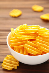 Potato chips on white bowl on brown wooden background.