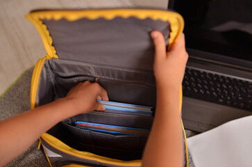 Hands of a child collect books in a school backpack. School, distance learning.