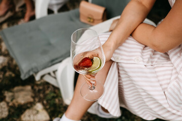 Woman holding a glass of water with strawberry and lime, outdoors, at a party.