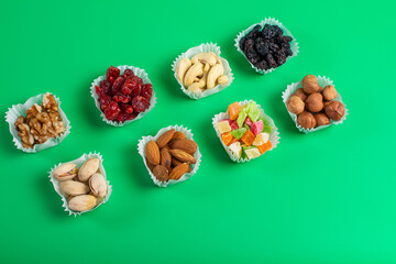 A serving of assorted candied fruit, dried cherries, almonds, raisins, walnuts and hazelnuts in paper muffin cups on a green background.