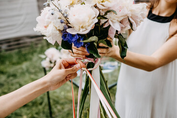Female hands holding and tying a bouquet of flowers with colorful ribbons. Florist making an...