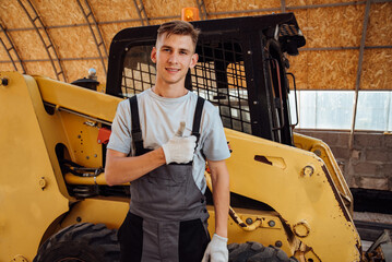 Fototapeta na wymiar Portrait of a handsome young farmer standing in overalls and smiling at the camera, on a tractor background.