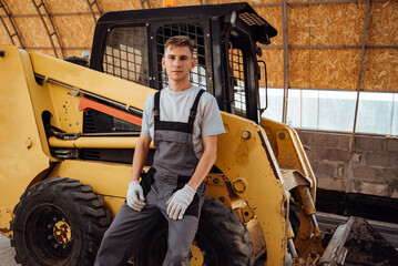Fototapeta na wymiar Portrait of a handsome young farmer standing in overalls and smiling at the camera, on a tractor background.