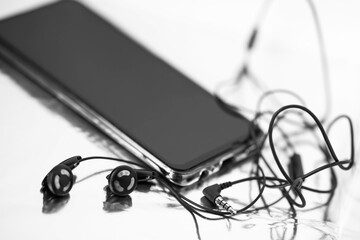 black-and-white image of a smartphone and headphones with wires