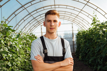 Portrait of a young male farmer in overalls in a greenhouse