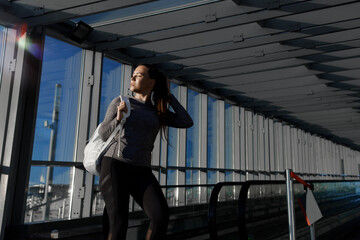 Portrait of young beautiful girl in trendy black leggings, T-shirt and backpack. Model in fashion sportswear on urban background on a sunny summer day.