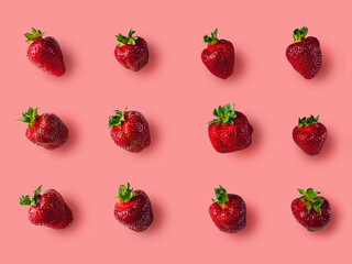 Ripe juicy red strawberries with green petals lie on a pink background.
