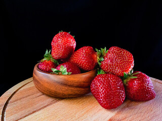 Strawberries on a black background. Ripe juicy red strawberries lie in a wooden bowl on a wooden 
cutting board.