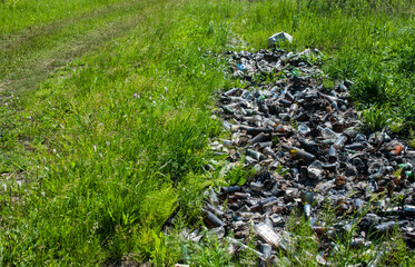 Garbage dump of burnt glass bottles on a green grass field