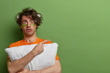 Horizontal shot of scared hipster guy indicates with fore finger aside, demonstrates something...