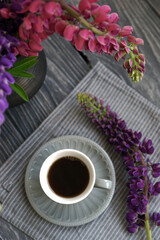 Small mug with black coffee and lupins on a wooden table