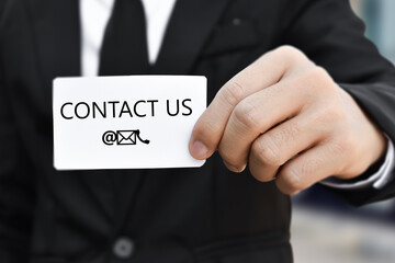 Businessman hand holding business card with the message contact us. Idea for customer support hotline people connect