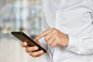 Close-up of male hand using smartphone. Businessman  touch mobile phone with bokeh background. Selective focus on hand.