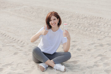 Fototapeta na wymiar Young woman drinking water sitting on the beach. Healthy Lifestyle. Healthcare. Drinks. Health, Beauty, Diet Concept. Healthy Eating. 