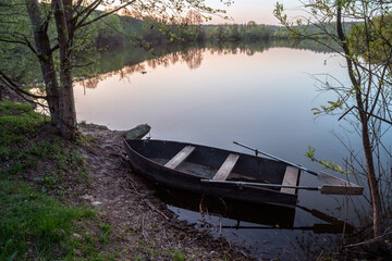Small boat with oars near the riverbank at sunset. Selective focus.