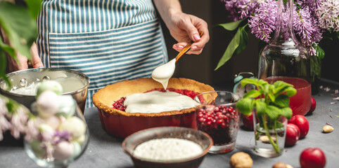 Cooking homemade cranberry pie. Female pastry chef is adding of sour cream with spoon to a baked tart with lingonberries