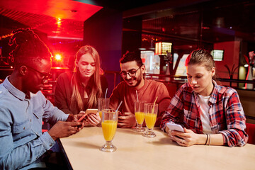 Group of four young intercultural friends in casualwear using mobile gadgets