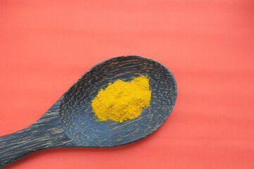 Fototapeta na wymiar turmeric on a wooden spoon on a red-orange background