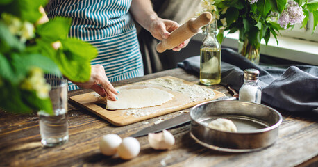 The woman is rolling out fresh dough for making pasta in a cozy atmosphere. Concept of cooking delicious food at home