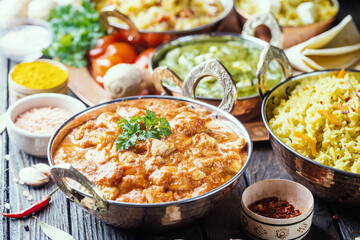 Different bowls with assorted indian food on dark wooden background. Dishes and appetizers of indian cuisine. Chicken, curry rice, lentils, paneer, chapati and spices.