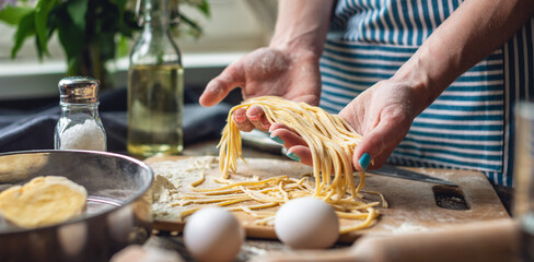 Woman is carefully holding raw homemade noodles in her hands. Process of cooking handmade pasta in...