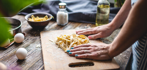 Woman is carefully sprinkling flour on fresh homemade noodles. Concept of cooking handmade pasta in a cozy atmosphere