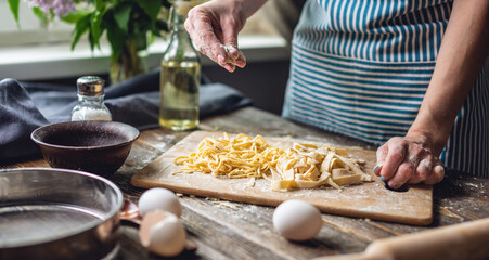 Woman is carefully sprinkling flour on fresh homemade noodles. Concept of cooking handmade pasta in a cozy atmosphere