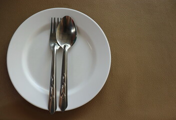 An empty white plate with a spoon and fork placed on a brown tableware