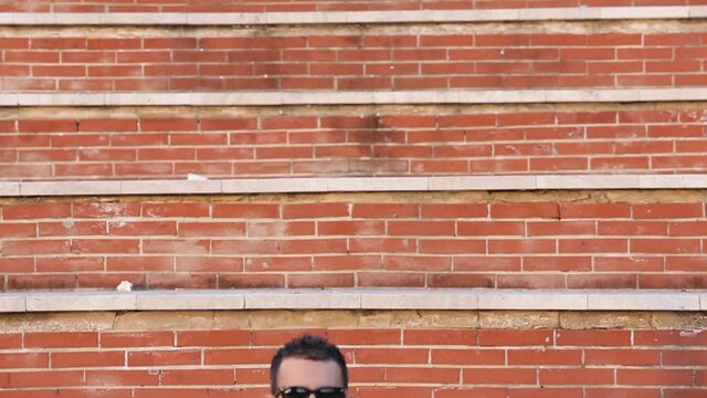Ragazzo in giacca e occhiali da sole si diverte a ballare in un acclimata di mattoncini rossi