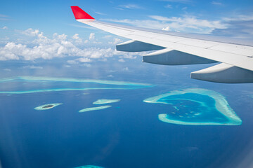 Naklejka na ściany i meble Airplane window with beautiful Maldives island view. Luxury summer holiday travel tourism background, view from airplane window. Atolls and islands with amazing tropical sea
