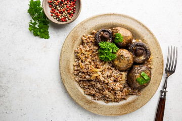 Buckwheat porridge with mushrooms in a plate on white table, top view