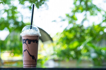 Cold cocoa in plastic glasses with the backdrop bokeh of green leaves sunlight.