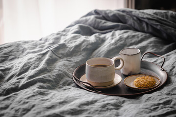 Morning coffee on vintage metal tray in bed with grey sheet and pillows.