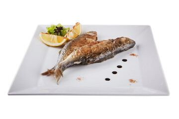 Grilled mackerel rests on a white plate. The fish is decorated with lemon.