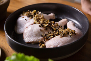 Raw chicken legs on a black plate marinated with garlic, pepper, meat with ingredients for cooking.