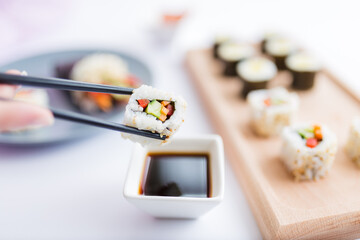 Close up of woman holding sushi roll with chopsticks above bowl full of soy sauce. Healthy traditional japanese meal concept.