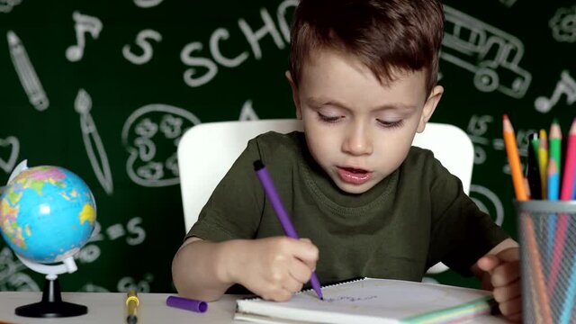 Preschooler boy making school homework. School boy with happy face expression near desk with school supplies. Education. Education first. School concept.