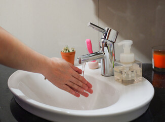 Light-skinned Asian woman rinsing hands in the bathroom sink. Shows hygiene and cleanliness for virus or bacterial spread prevention