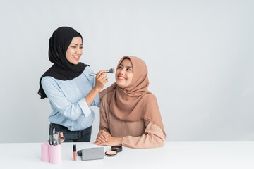 woman applying make up to young beautiful female wearing hijab