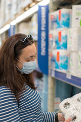 Woman in medical mask choosing goods in a store. Concept of shopping during quarantine at covid-19 pandemic. shopping at the time of the coronavirus. Beautiful young women in a flu mask