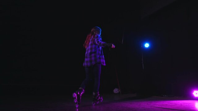 Pretty girl professionally skating on front and rear wheels, spinning in studio blue pink flood lights. Healthy lifestyle sport hobby concept. Teenager on stage rides roller skates performing element