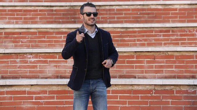 Uomo moro con giacca e occhiali da sole si muove ballando tra i gradini a mattoncini rossi