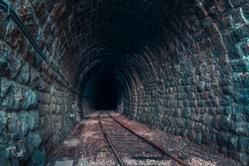 Curved stone railway tunnel with railroad tracks. Endless view in dark area