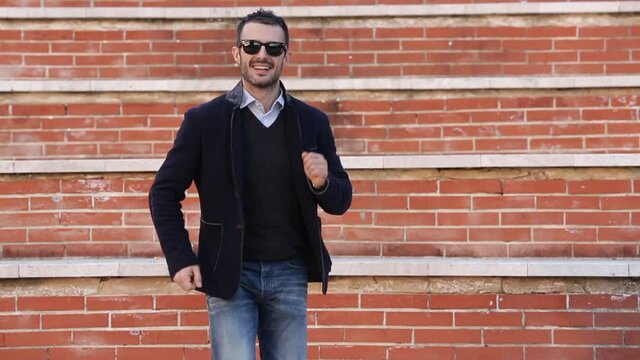 Uomo moro con giacca e occhiali da sole si muove ballando tra i gradini a mattoncini rossi