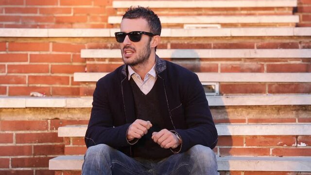 Uomo moro con giacca e occhiali da sole si muove ballando tra i gradini a mattoncini rossi