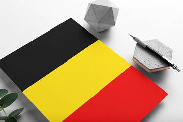 Belgium flag on minimalist paper background. National invitation letter with stylish pen on stone. Communication concept.