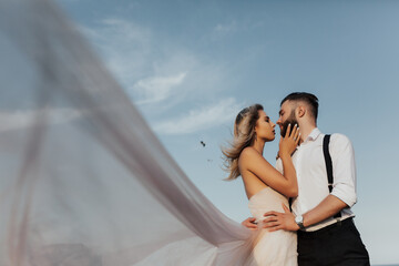 Portrait of couple looking each other on a background of blue sky. Bride and groom kisses tenderly in the shadow of a flying veil .Beautiful picture. Copy space.