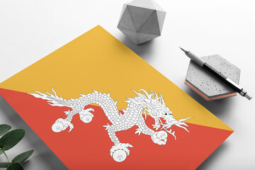 Bhutan flag on minimalist paper background. National invitation letter with stylish pen on stone. Communication concept.