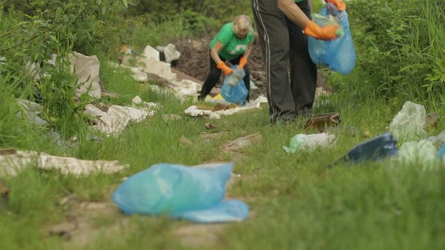 Team of nature activists in eco T-shirts picking up plastic trash in park. Recycle, earth pollution
