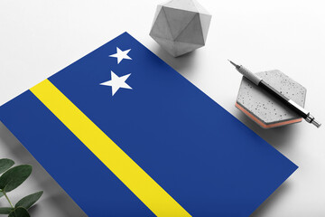Curacao flag on minimalist paper background. National invitation letter with stylish pen on stone. Communication concept.